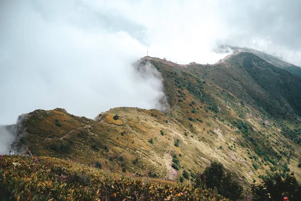 Kafkasya tepesinin panoramik manzarası bulutlarla kaplı, yürüyüş yolu, yamaç, gri gökyüzü, sonbahar, serinlik, uzaklarda yürüyen turistler, sarı ve yeşil çimenler, çalılar