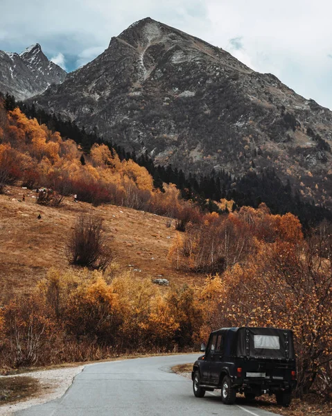 Dağlarda bir dağ yolu, ağaçlar ve bir araba olan sonbahar manzarası. Dağdaki sarı ağaçlar. Siyah araba otoyolun kenarına park edilmiş. Siyah dağ. Dombay