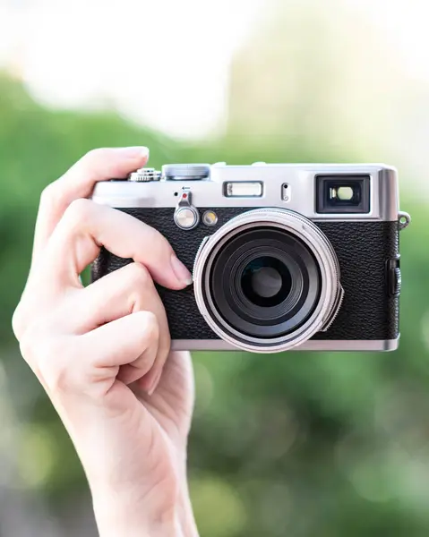一个老式胶卷相机的闭锁 年轻的 白色的 女性的手拿着相机在模糊的绿色背景与Bokeh 手从侧面拿着相机 镜头对准了摄影师 眼平射箭 — 图库照片