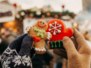 Eldivenli kadın ve erkek eller Noel kurabiyelerini Noel pazarının arka planında tutuyor. Yakın plan, zencefilli kurabiye adam, kremalı kurabiye. Yeni yıl havası, Noel, Prag 'da aşık çift, Çek Cumhuriyeti
