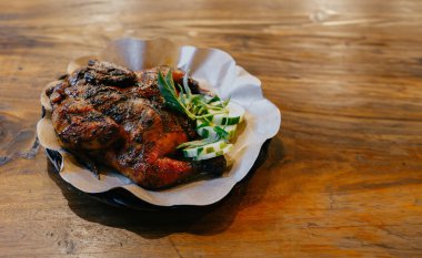 Kahverengi yağa dayanıklı tabakta salatalık dilimleri ve fesleğen yapraklı ızgara tavuk. Ahşap masa arkaplanlı yatay üst görünüm.