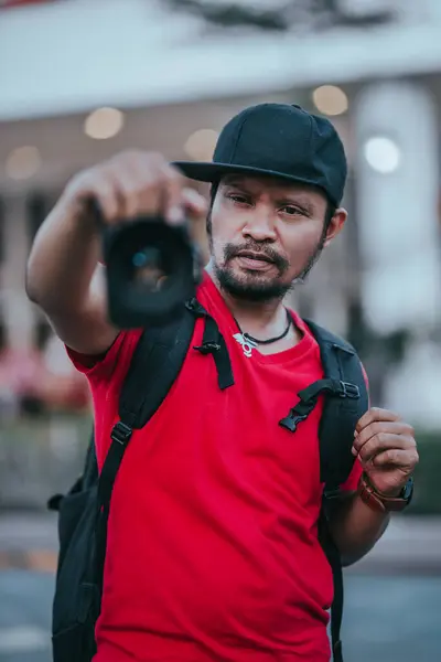 インドネシアの男性写真家で 黒い帽子と赤いTシャツを被ったひげとひげを抱え 前景がぼやけている — ストック写真