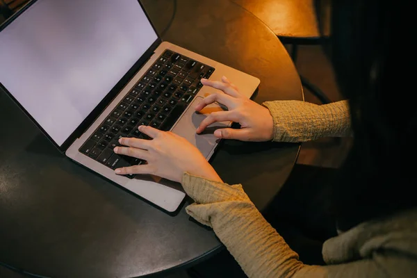 Woman using laptop, searching the web, browsing information, having a workplace at home with warm lighting around.