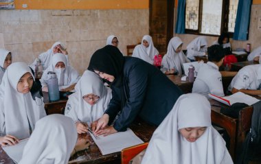 Surabaya, Endonezya, 29 Mayıs 2023 - Asyalı Müslüman kadın öğretmen çocuklara lisede resim dersi veriyor. Okulda öğretim ve öğrenim süreci kavramı.