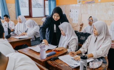 Surabaya, Endonezya, 29 Mayıs 2023 - Asyalı Müslüman kadın öğretmen çocuklara lisede resim dersi veriyor. Okulda öğretim ve öğrenim süreci kavramı.