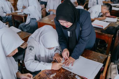 Surabaya, Endonezya, 29 Mayıs 2023 - Asyalı Müslüman kadın öğretmen çocuklara lisede resim dersi veriyor. Okulda öğretim ve öğrenim süreci kavramı.