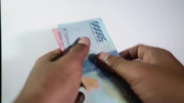 Beyaz arka planda 100.000 ve 50.000 rupia 'lık Endonezya para birimini elinde tutan bir adamın yakın çekimi. Seçici odak 4K video kaydı.