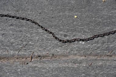 Garaj yolundaki gri asfaltta metal bir zincir var.