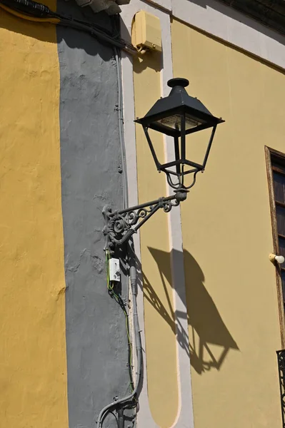 a vertical shot of a yellow lamp on a street with a yellow wall in the background