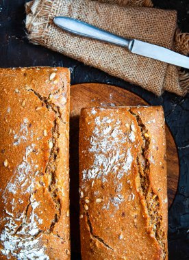 Ev yapımı taze pişmiş tam tahıllı çavdar ekmeği ve siyah arka planda tohumlar..