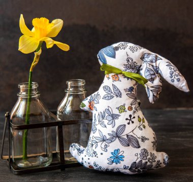 Cam şişelerde güzel sarı bir çiçeğin yanına yerleştirilmiş sevimli bir kumaş tavşan. Bahar dekorasyonu için ideal.