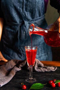 A woman's hand pours cherry liqueur into a glass. Homemade cherry liqueur. clipart