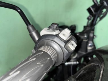 Detaylı bir görüntüde motosikletin sol gidonu, ışıkların birleşik beyaz kontrol düğmeleriyle birlikte siyah sapı vurgulanıyor ve dönüş sinyalleri veriliyor..
