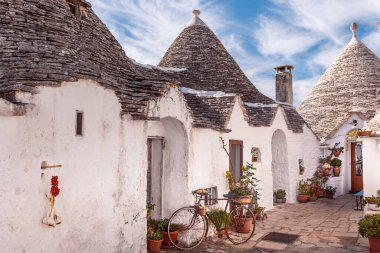 Trulli evleri bitkiler ve çiçeklerle süslenmiş, bir demet sarımsak ve kiraz domatesleri duvarda asılı. Alberobello, Bari, İtalya