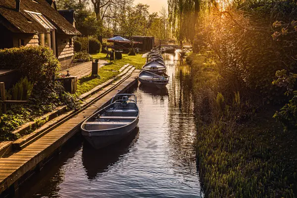 Güneş, Hollanda, Giethoorn 'da tekneleri ve resimli evleri olan bir idilyc kanalının üzerinde batıyor.