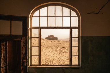 Namibya, Kolmanskop 'un ana binası Namib Çölü' nün sıcak ışığı altında bir pencereden geçmektedir. 1908 'de Almanlar tarafından elmas keşfi için kuruldu ve 1956' da terk edildi..