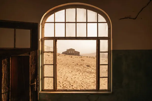 Namibya, Kolmanskop 'un ana binası Namib Çölü' nün sıcak ışığı altında bir pencereden geçmektedir. 1908 'de Almanlar tarafından elmas keşfi için kuruldu ve 1956' da terk edildi..