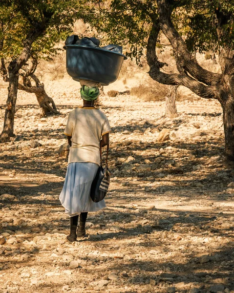 地元の女性は彼女の頭 エパパフォールズ クネンリージョン ナミビアの家で洗濯された服を運びます ロイヤリティフリーのストック画像