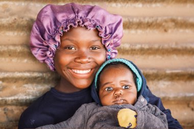 Young Lozi (Caprivian) woman wearing traditional headwear and her baby, Katutura, Windhoek, Namibia. Katutura is a township created in the 1950s to segregate the black population of Windhoek. clipart