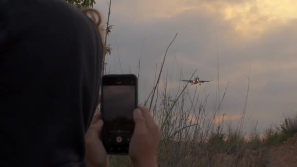 スウェットシャツに認識できないティーンエイジャーは 飛行機が着陸ギアを延長するために来るので 携帯電話上のビデオを記録します — ストック動画