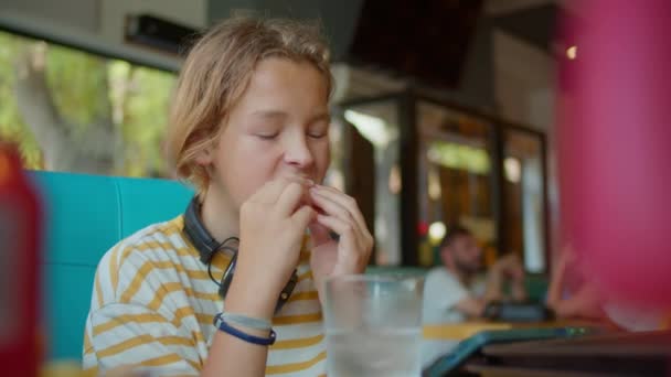 Letni Chłopiec Pasiastej Koszuli Korzysta Hot Doga Kawiarni Pochłoniętego Smartfonem — Wideo stockowe