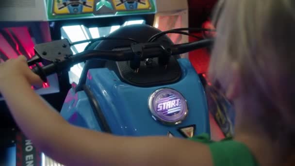 6岁的女孩在街机上骑摩托车 按下起步键 从后面和上面观看整个游戏 — 图库视频影像