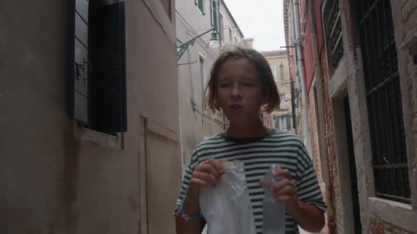 慢动作 一个少年徘徊在意大利威尼斯狭窄的街道上 他喜欢吃包里的小吃 一边在历史性的小巷里漫步一边喝水 — 图库视频影像