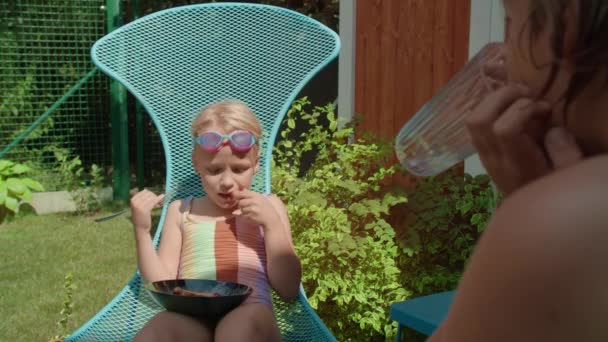 Egy Fürdőruhás Fiatal Lány Élvezi Kolbászos Ételt Miközben Bátyja Mellette — Stock videók
