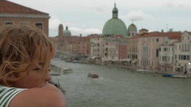 Çizgili tişörtlü bir çocuğun profili Venedik ikonik binalara bakıyor. Aralarında San Simeone Piccolo kilisesi de var.