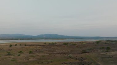 Sinematik dron hareketiyle yakalanan bu hava manzarası dalgalı arazi, dağınık bitki örtüsü ve alacakaranlığın bastırılmış tonlarını yansıtan durgun sularıyla sakin bir göl manzarasını gözler önüne seriyor.