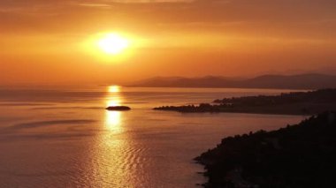 Gün batımında sinemada geriye doğru çekilen bir dronun hava görüntüsü güneşin nefes kesen manzarasını canlı, altın bir gökyüzü ile ufka batarken gösteriyor.