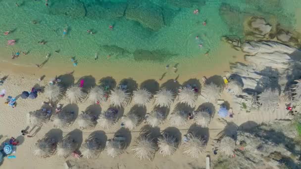 ドローンカメラで直接撮影された活気に満ちたビーチシーンの空中撮影で 多くの人が透明なターコイズの水を点検し わら傘の陰でリラックスしています — ストック動画