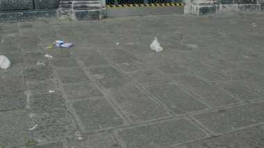 Kağıt, plastik gibi atıklar, kirlilik sorunlarını ve çöpün kentsel çevre üzerindeki çevresel etkilerini vurgulayan taş döşeli kentsel alana saçılmış durumda.