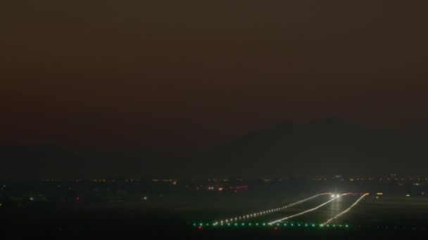 飛行機は夜に離陸し その明るい着陸ライトは暗い山の背景に滑走路を照らします — ストック動画