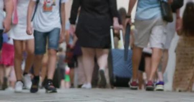 Şehir caddesi boyunca yürüyen, bavullarını taşıyan birkaç kişinin bavulları üzerinde durduğu yakın çekim, bulanık bir görüntü.