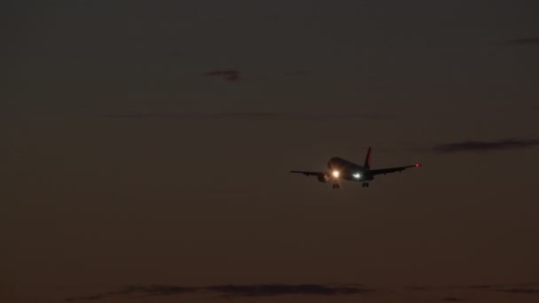 着陸装置が解放され ライトが点灯する飛行機は 勾配色と雲で明るい空の背景に降下しています — ストック動画