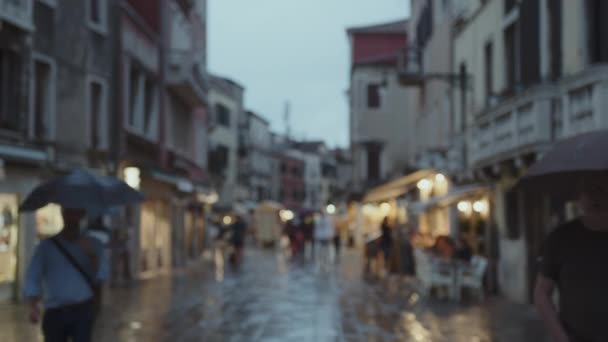市内の雨の夜のぼやけたイメージ 傘の下の歩行者と湿った表面を反映した街灯 ヴェネツィア イタリア — ストック動画