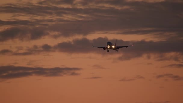 착륙을 준비하는 황혼에 오렌지 구름의 배경에 항공기 — 비디오