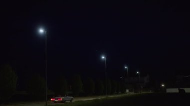 Geceleri, sokak lambaları, hareket halindeki bir trenin kırmızı ışıklarının göründüğü ve evlerin belli belirsiz çizgilerinin görülebildiği bir bölümü aydınlatıyor.