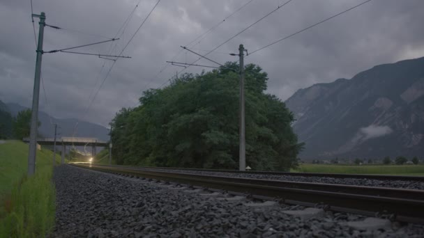 黄昏时分 火车的前灯在铁轨上闪闪发光 铁路线在上方 山脉在远处被云彩遮掩 — 图库视频影像