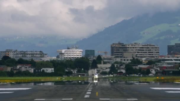 小さな飛行機が滑走路から離れ 昼間のバックグラウンドに都市の建物と間違った丘があります — ストック動画