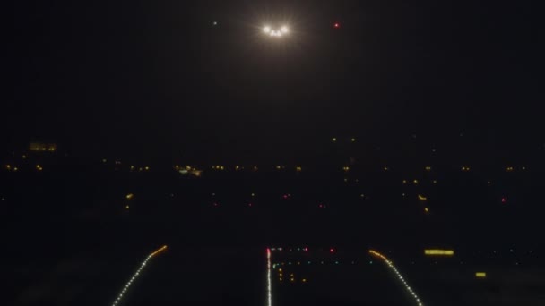 飛行機の明るい着陸ライトは 夜間着陸のためのライトが並ぶ滑走路に向かって下降するように見えます — ストック動画