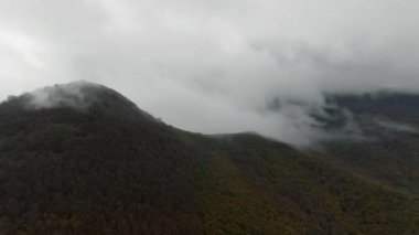 Yeşil dağ yamaçlarının havadan görünüşü gri bulutlar ve sisten oluşan bir battaniyeye yükselir.