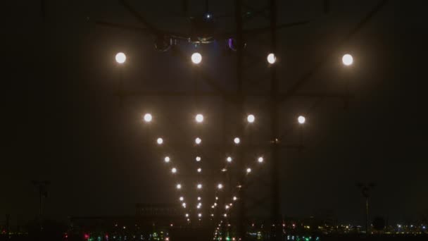夜間にアプローチ照明システムの中心に飛行機が捕獲され 滑走路に向かって明るい着陸灯が点灯し 周囲の空港ライトの背景に設定されます — ストック動画