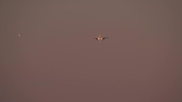 ヘッドライトが点灯し 着陸装置が放出された飛行機の前景は トワイライト空を飛行し 別のほとんど区別できない飛行機が遠くに見えます — ストック動画