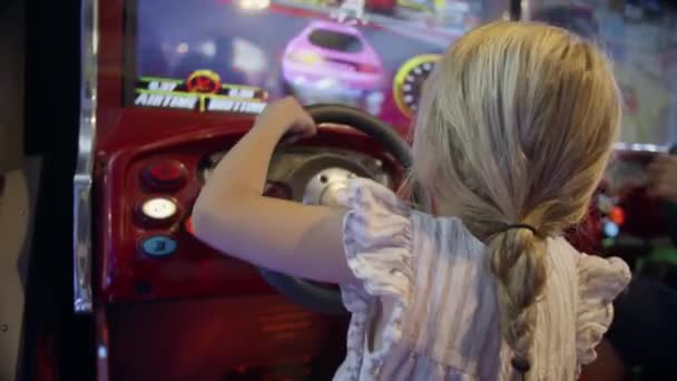 骑着马尾辫玩赛车视频游戏的金发孩子 手扶方向盘在拱廊上 — 图库视频影像