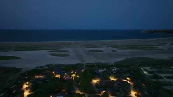 一架朝相反方向飞去的无人驾驶飞机捕捉到了一个沿海村庄的夜灯 那里的街道通向海滩 还有大海 — 图库视频影像