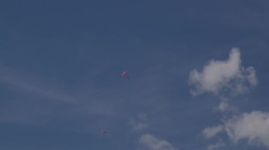 Turuncu ve pembe paraşütlü üç paraşütçü açık bir günde paraşüt yaparak mavi gökyüzünde süzülüyor.