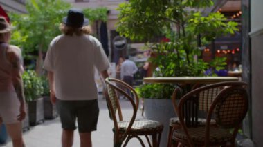 Budapeşte, Macaristan 'da Kiraly Caddesi' ndeki hasır sandalyeli kaldırım kafesi ön planda canlı yeşil bitkiler ve arka plandan geçen yayalar.