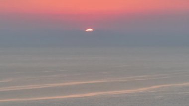 Güneşin hava görüntüsü sakin bir akşamda sislerle kaplı okyanusa yavaşça iniyor.